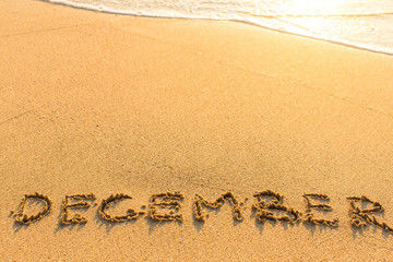 December - inscription on sand beach with the soft wave.