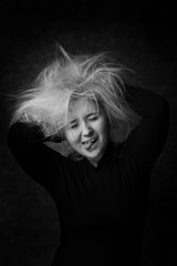 Sexy young woman putting hands in her disheveled hair. Sexy look in black and white portrait. Woman looking joking with puling out her tongle out.