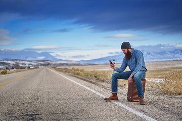 lost hitch hiker using smart phone on side of road