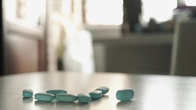 Blue pills being poured from the bottle on the table. Slow motion close up shot