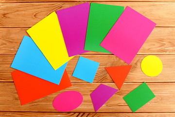 Colorful cardboard geometric shapes. Cut from cardboard triangle, square, oval, trapezoid, rectangle, circle. Children education concept. Sheets of colored paperboard on a wooden table