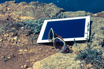 White digital tablet with dark empty screen on the rock mountain and rocky coast background.