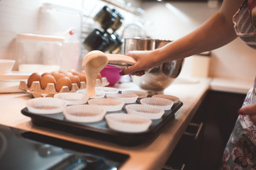 Woman cooking cupcakes closeup. Pouring batter in baking dish on table. Selective focus. - obrazy, fototapety, plakaty