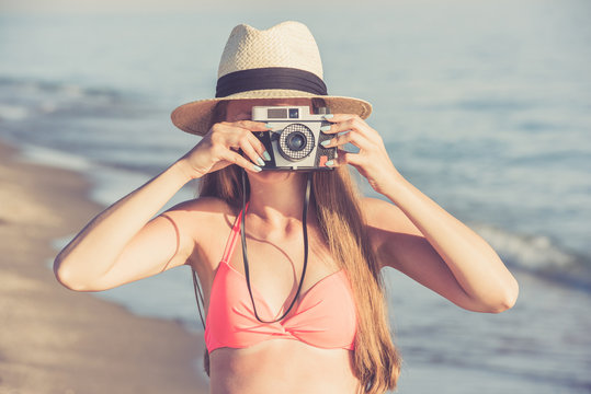 Young woman taking photo on the beach using retro camera