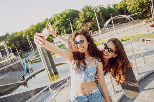 Young girls doing selfie with a skateboard.
