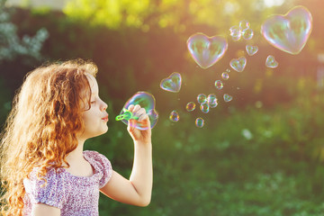 Little girl blowing soap bubbles, happy childhood concept.