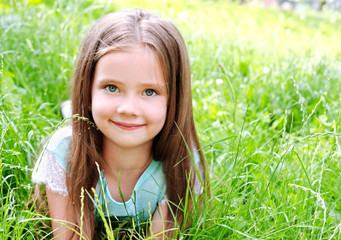 Adorable smiling little girl lying on grass in summer day