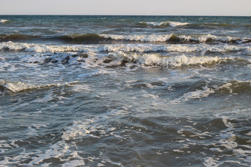 Sea surf waves with foam caps. Evening view from beach.