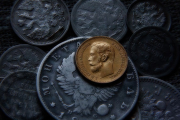 Eight silver and one gold Russian coin of the nineteenth century in the muffled light. Blurred...