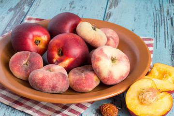  Fresh nectarines and peaches.   Fresh nectarines and peaches on a brown ceramic dish on a blue wooden background.