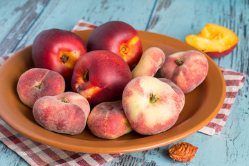  Fresh nectarines and peaches.   Fresh nectarines and peaches on a brown ceramic dish on a blue wooden background.