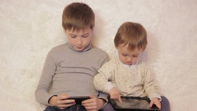 Children sitting on the couch playing on your tablet and phone to computer games