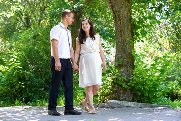 pregnant woman with husband walking in the city park, family portrait, summer season, green grass and trees