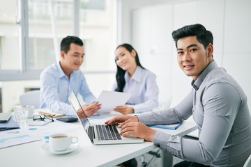 Fototapeta premium Portrait of young Vietnamese businessman working on laptop in office