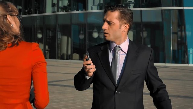 Slow motion. Young sexy businesswoman dissolve hair and flirt with businessman outdoor. Glass business centre building at the bg. Teal and orange steadicam shot.