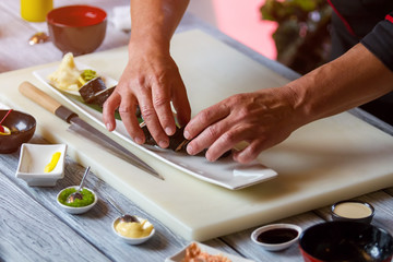 Obraz na płótnie Canvas Man's hands touch sushi rolls. Sushi plate on cooking board. Futomaki rolls in restaurant kitchen. Old and proven recipe.