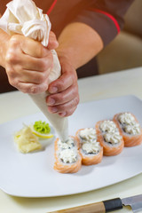 Sushi rolls on plate. Pastry bag in man's hands. Japanese dish with cream cheese. Appetizing uramaki rolls.
