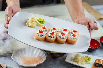 Obraz na płótnie Canvas Male hands hold sushi plate. Sushi rolls with caviar. Uramaki rolls served with spices. Appetizing dish made of seafood.