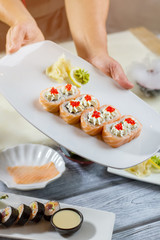 Man's hands hold sushi plate. Wasabi on lemon slice. Traditional uramaki rolls with caviar. Japanese dish for breakfast.