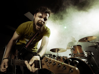 Rock band performs on stage. Guitarist, bass guitar and drums. The guitarist plays solo.
