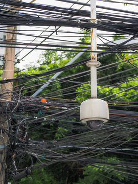 Old CCTV camera security hanging on chaos of cables and wire, Bangkok, Thailand