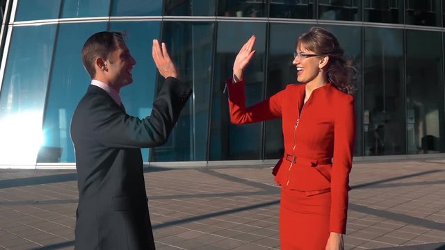 Slow motion: young sexy business woman in red suit with spectacles and men in black suit give five outdoor at the business centre building bg. Teal orange. Steadicam middle shooting.