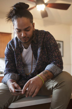 Young man using smartphone while sitting on kitchen countertop