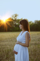 Fototapeta na wymiar Pregnant woman in white dress watching the sunset outdoors