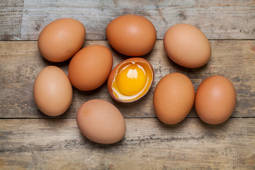whole and broken raw brown eggs closeup on wood table