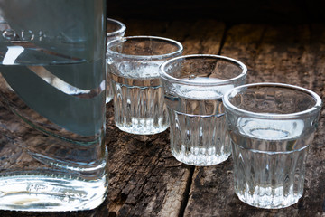 bottle of vodka and shot glasses on a wooden background close up