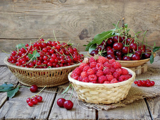 Fresh fruit and berries in baskets on wooden background - red currants, raspberries, cherries - rustic foto