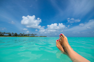 Fototapeta na wymiar Close-up of female foot in the blue water on the tropical beach.
