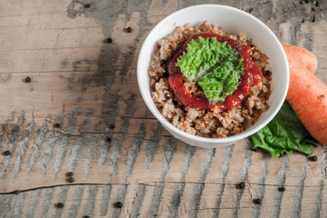 Buckwheat porridge with tomato sauce and leaf salad in a white bowl on a wooden table next to a ceramic bowl with dish is carrots or sliced carrot. Food background. Nice and tasty atmosphere.