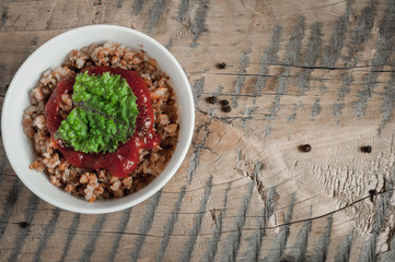 Buckwheat porridge with tomato sauce and leaf salad in a white bowl on a wooden table next to a ceramic bowl with dish is carrots or sliced carrot. Food background. Nice and tasty atmosphere.