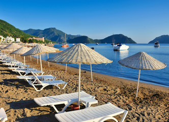 Beach with sunshades and sunbeds against the backdrop of the picturesque bay of blue sea and mountains