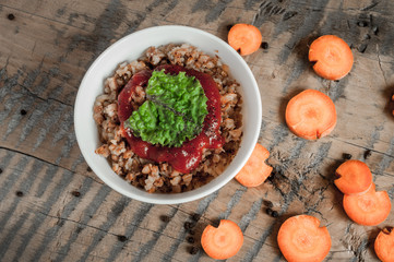 Buckwheat porridge with tomato sauce and leaf salad in a white bowl on a wooden table next to a ceramic bowl with dish is carrots or sliced carrot. Food background. Nice and tasty atmosphere.