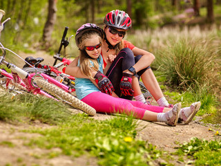 Obraz premium Bikes cycling family. Happy mother and daughter are sitting on road near bicycles. Cycle racing concept.