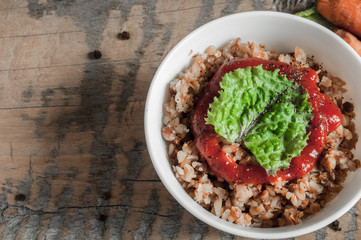 Buckwheat porridge with tomato sauce and leaf salad in a white bowl on a wooden table next to a ceramic bowl with dish is carrots or sliced carrot. Food background. Nice and tasty atmosphere.