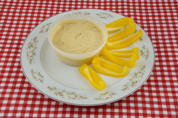 Healthy Hummus dip and yellow bell pepper slices on white plate on table