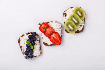 Set sweet sandwiches with cream-cheese and fresh berries and fruit over a white background . Top view. healthy breakfast.selective focus.