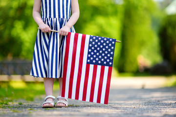 Adorable little girl holding american flag outdoors on beautiful summer day