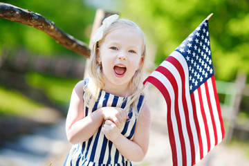 Adorable little girl holding american flag outdoors on beautiful summer day