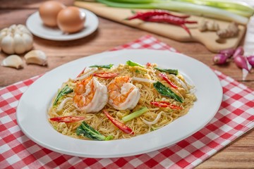 Plate of fried vermicelli with shrimps and herbs on the table in restaurant