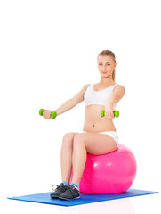 Beautiful young girl doing exercises with fit ball and dumbbells isolated over white background