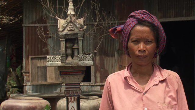 Cambodian woman in head cloth posing for portrait near small shrine
