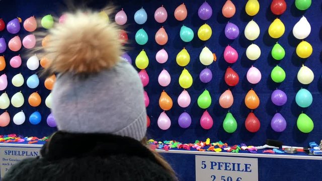 Kid playing carnival dart game to attempt to win a prize by popping balloons.