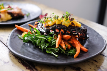 Roasted pork ribs with potato and herbs on black plate