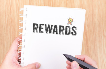 Rewards word on white ring binder notebook with hand holding pen