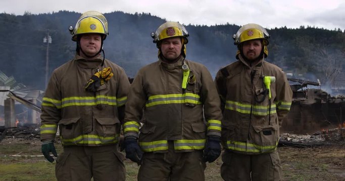 Three firemen stand in front of the smoldering ruins of a house