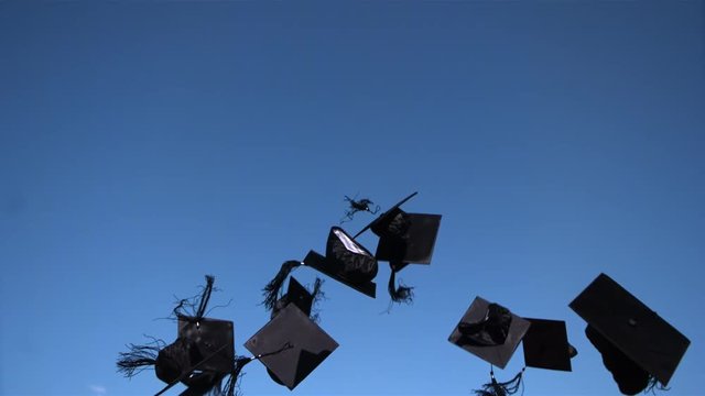 Ultra-slow motion shot of academic caps sailing into blue sky on graduation day